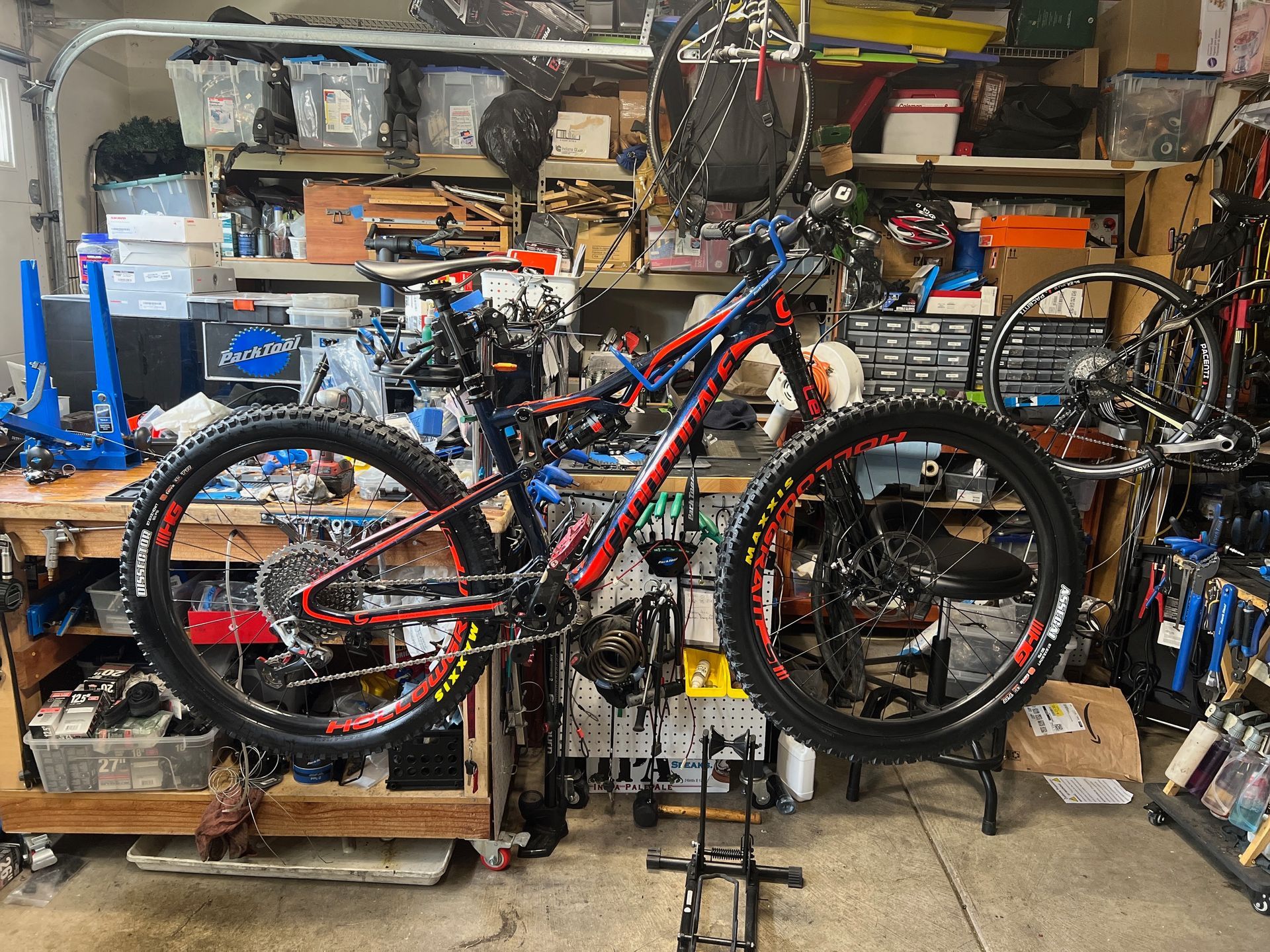 Mountain bike in repair stand in a cluttered workshop with tools and parts.
