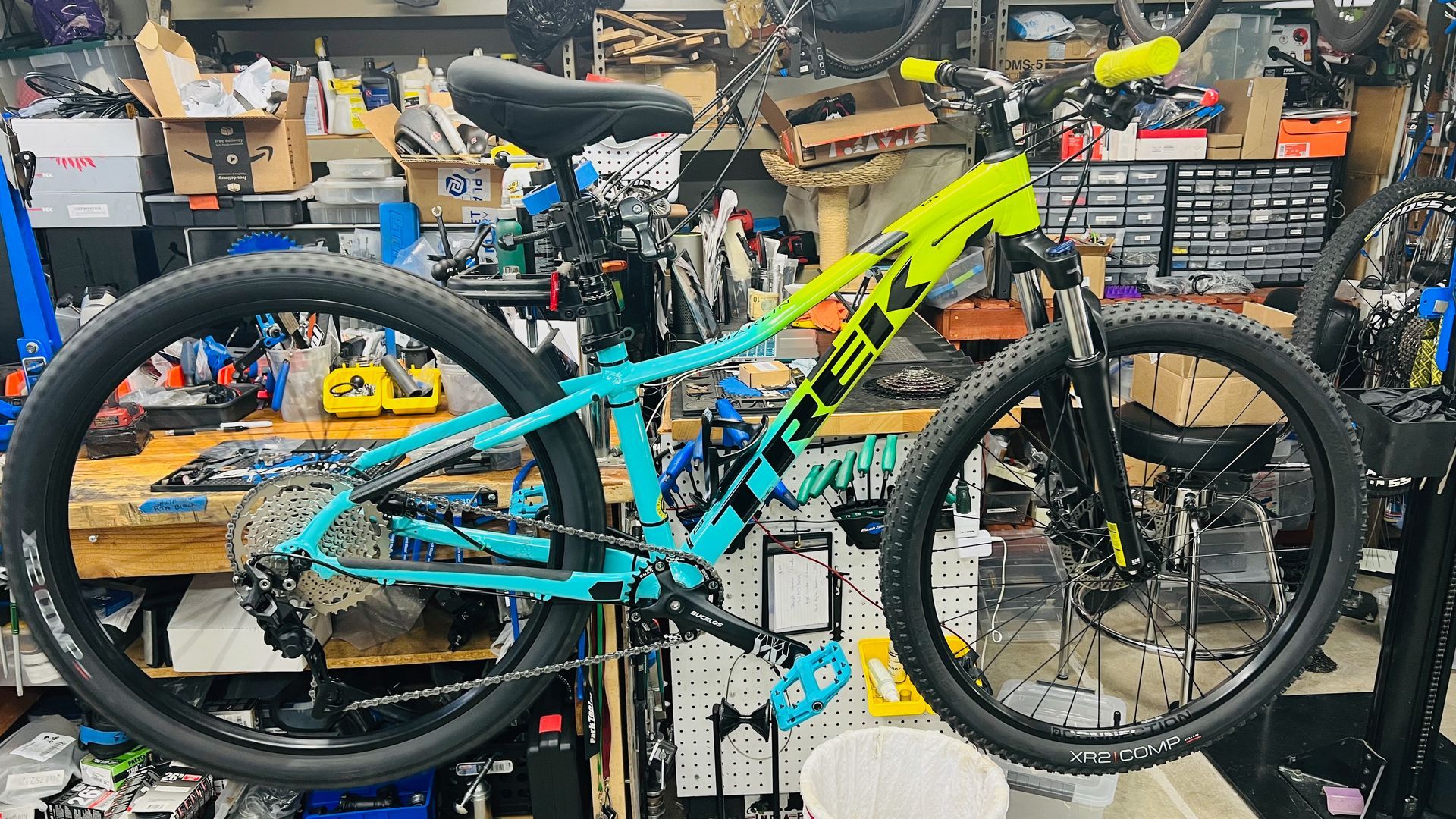 A teal and yellow mountain bike in a cluttered workshop, angled slightly to the side.