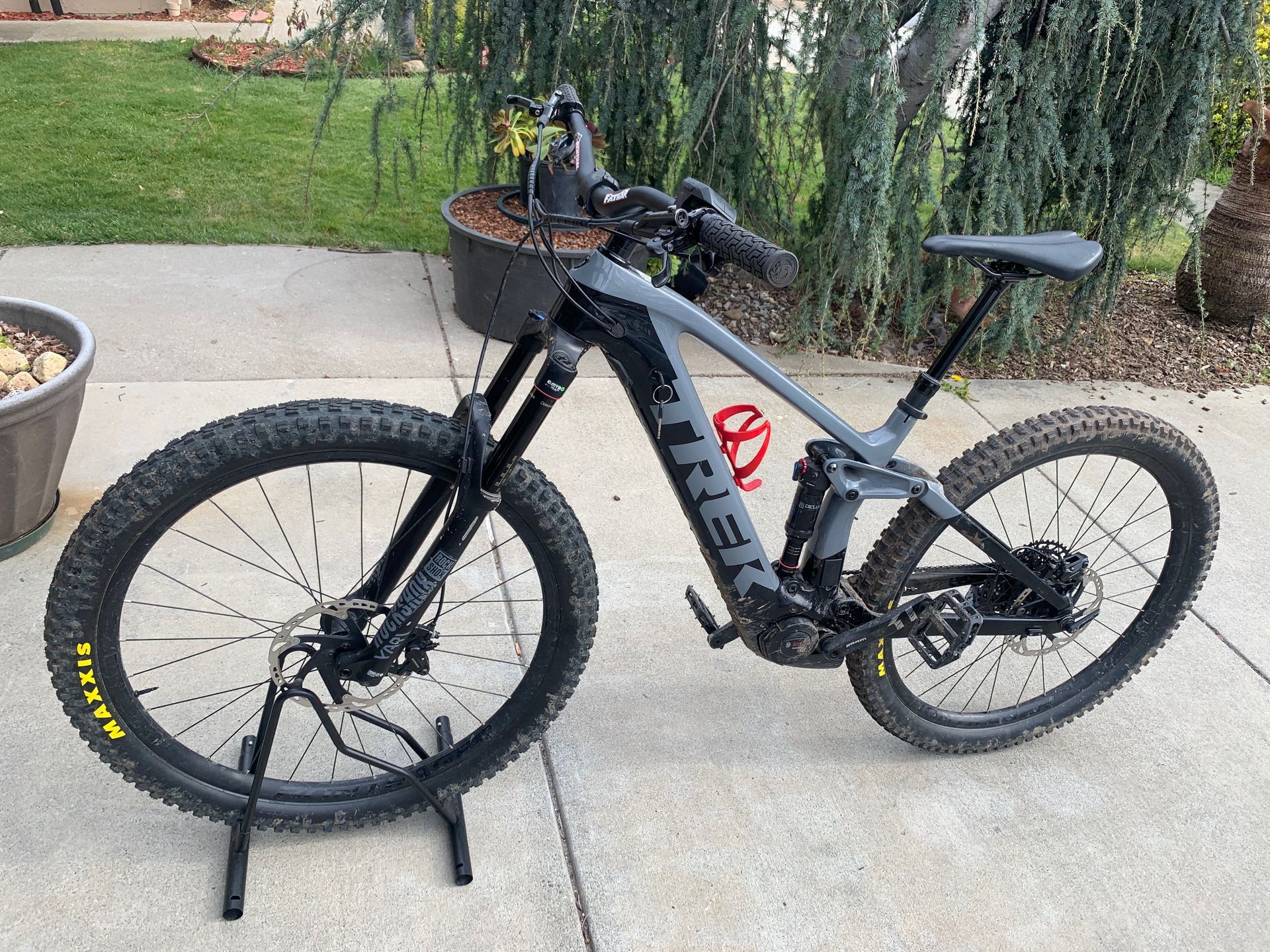 Gray and black electric mountain bike on a stand outdoors with a grassy background.