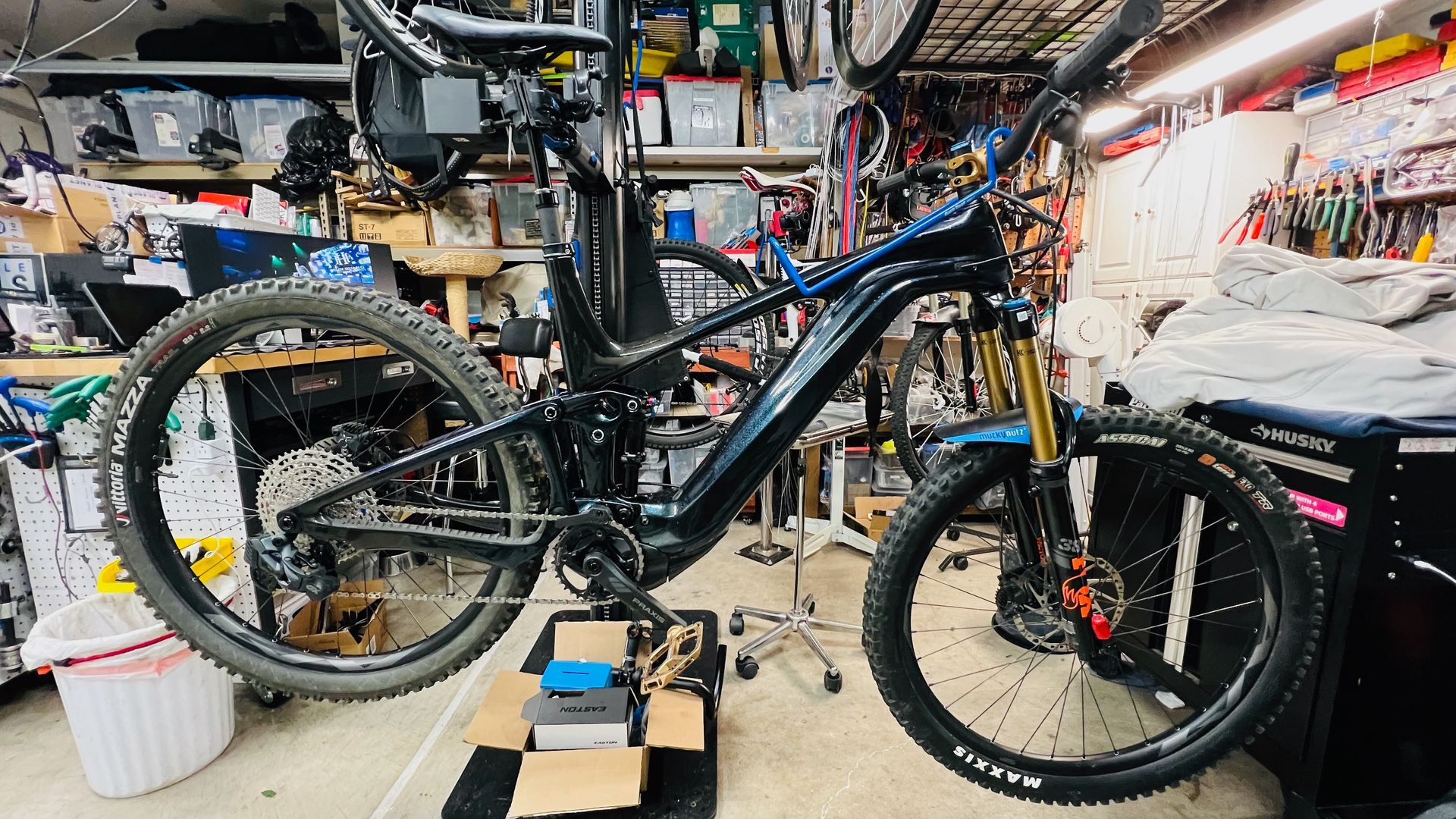 Black mountain bike in a cluttered garage, being worked on.