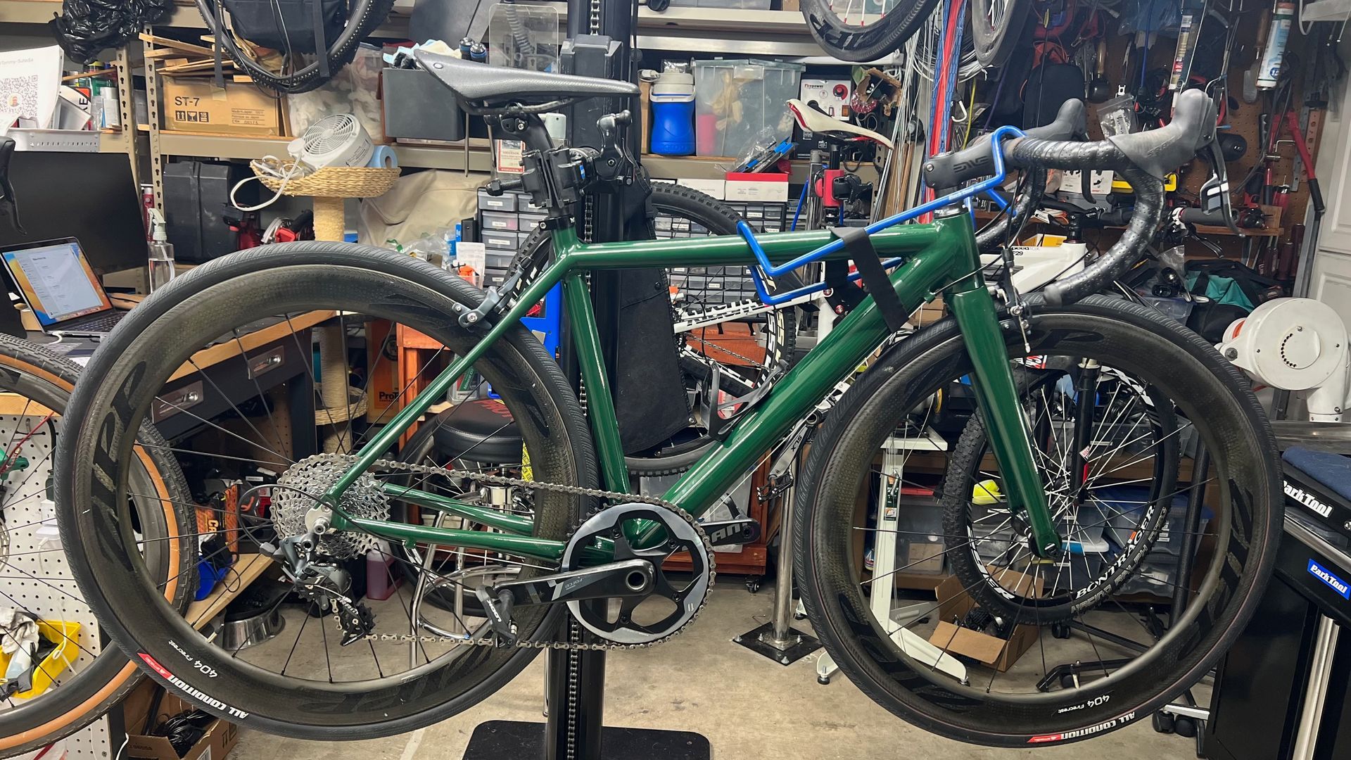 Green road bike on a repair stand, dark wheels, set in a cluttered shop.