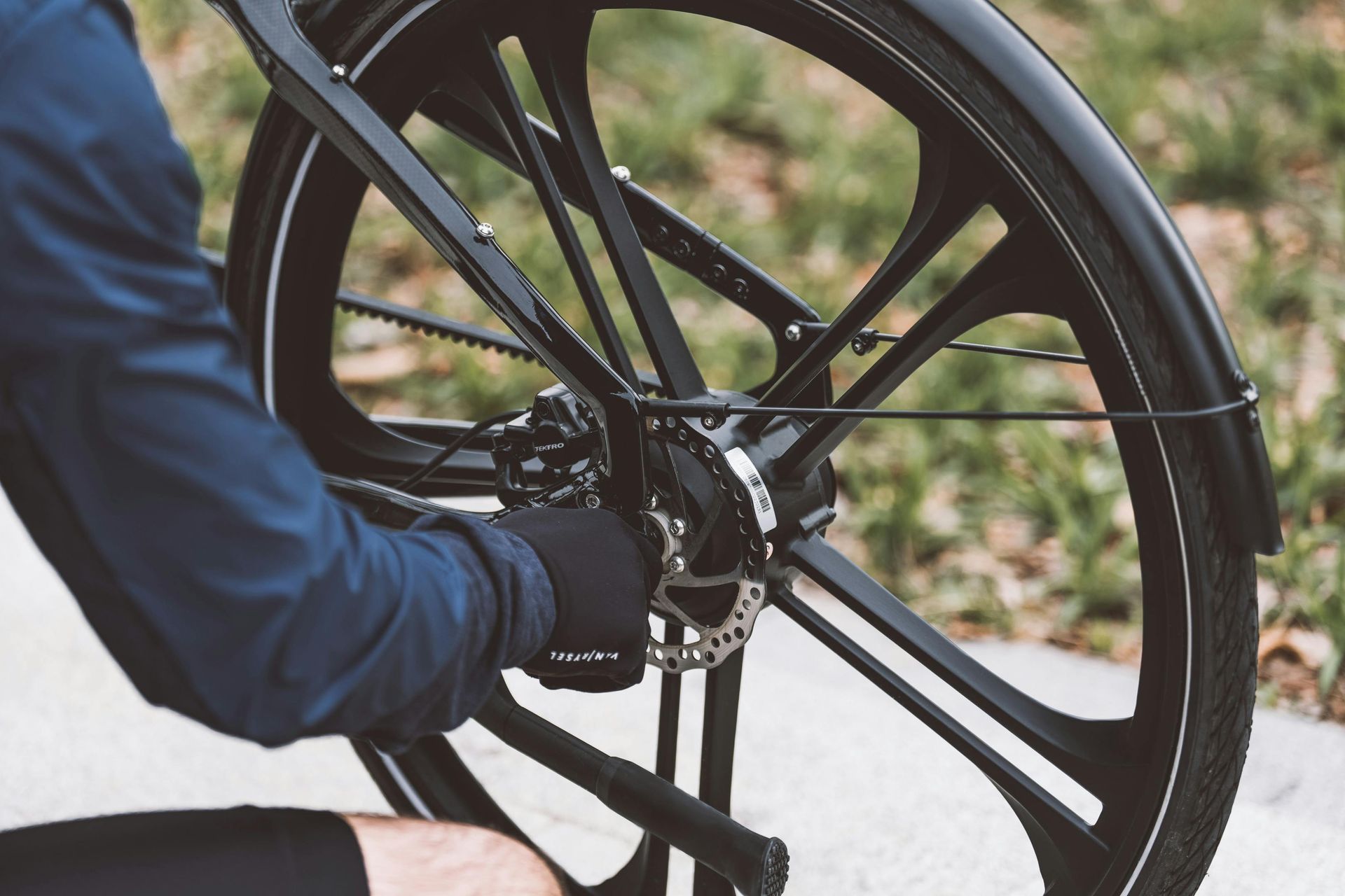 A person wearing a blue jacket and black glove adjusting the disc brake on a black bicycle wheel.