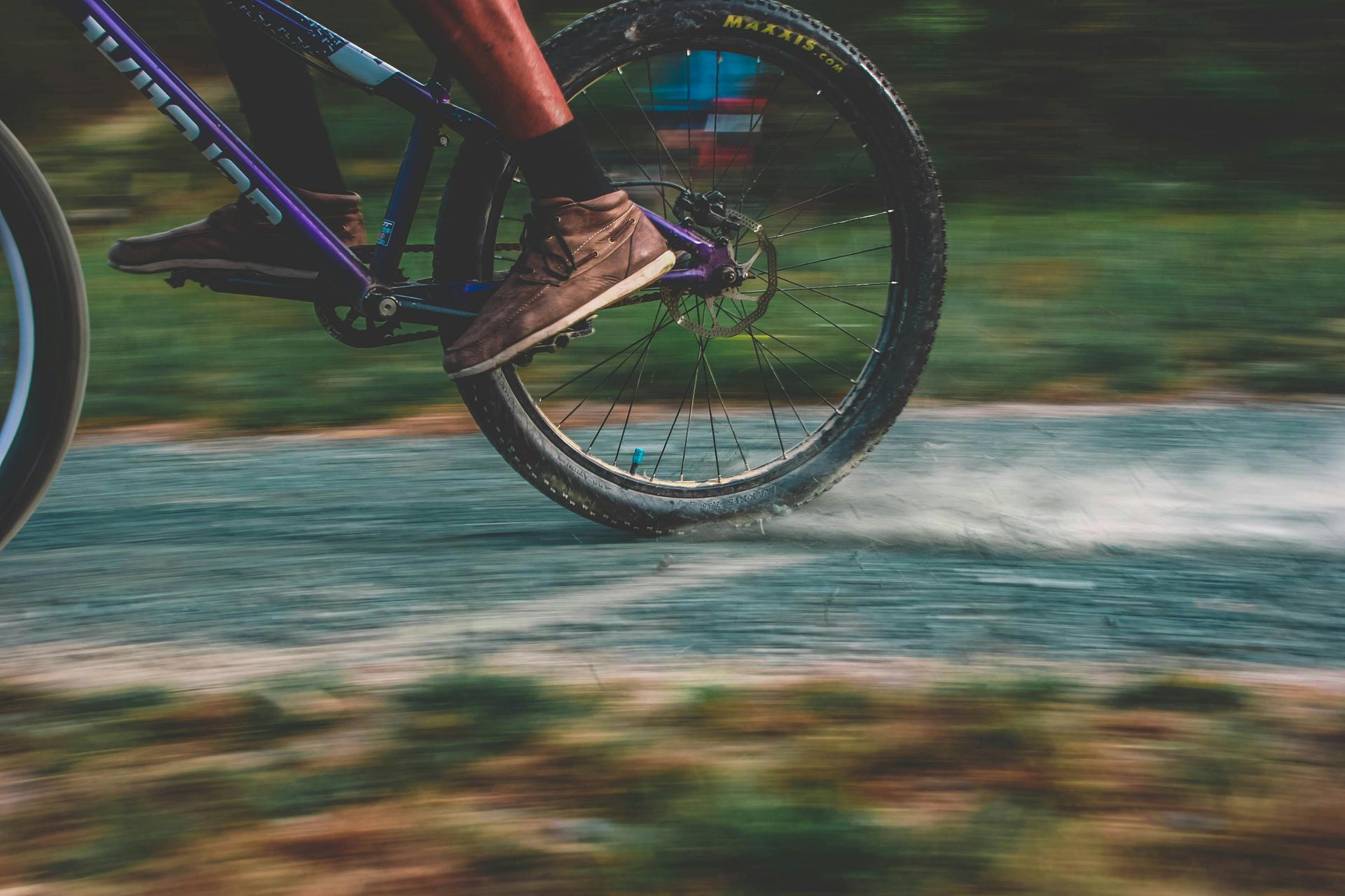 A close-up of a mountain bike wheel and rider's feet moving fast over a dirt track, creating a dust trail.