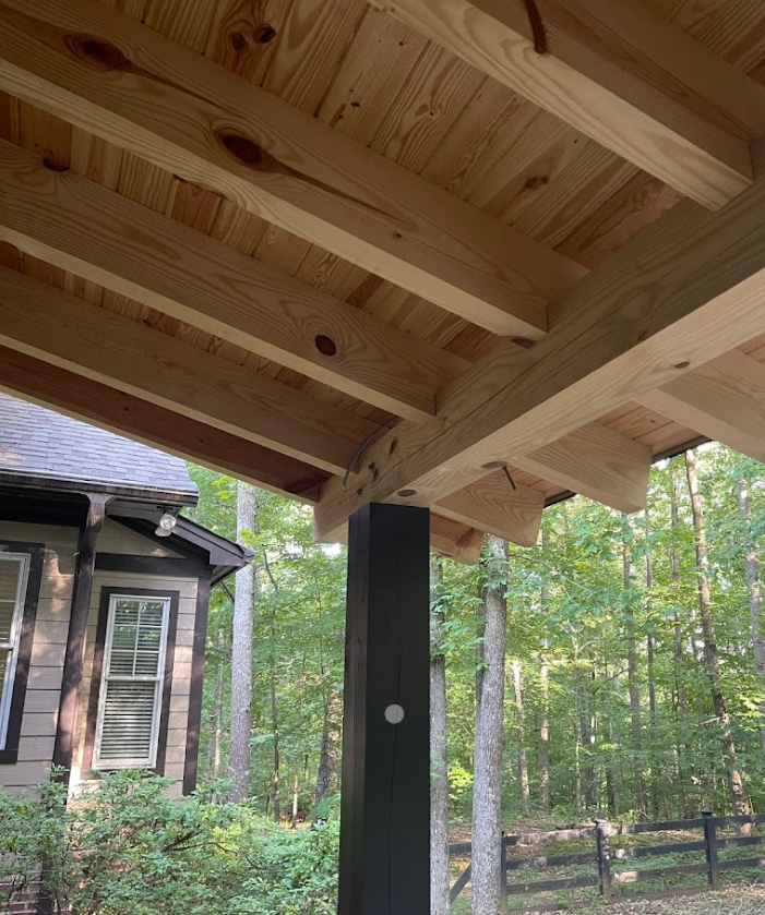 A wooden roof is being built over a porch with a house in the background.