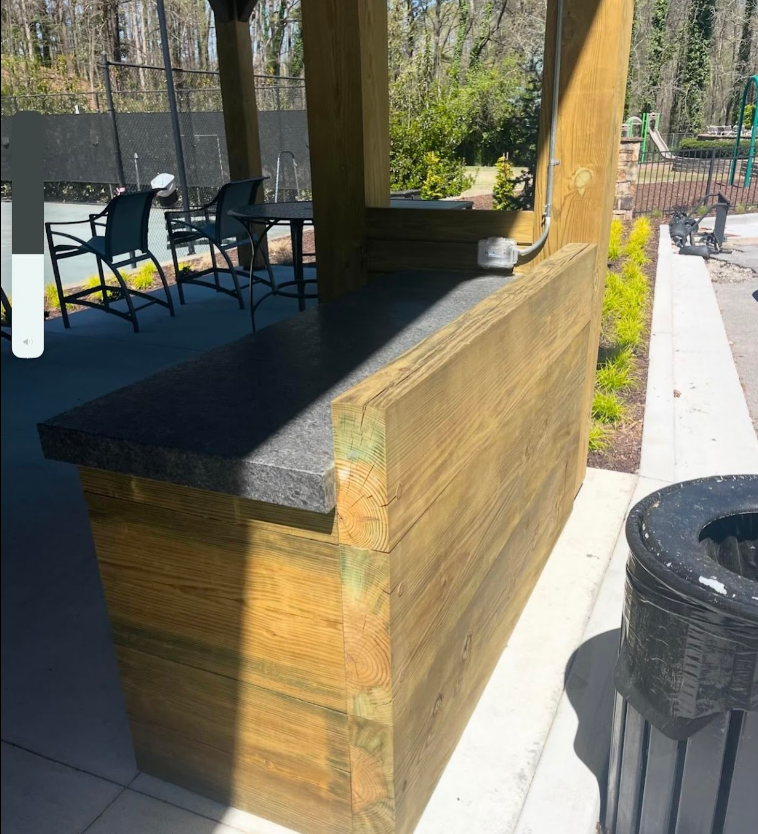 A wooden bar with a black counter top sits under a covered area with tables and chairs