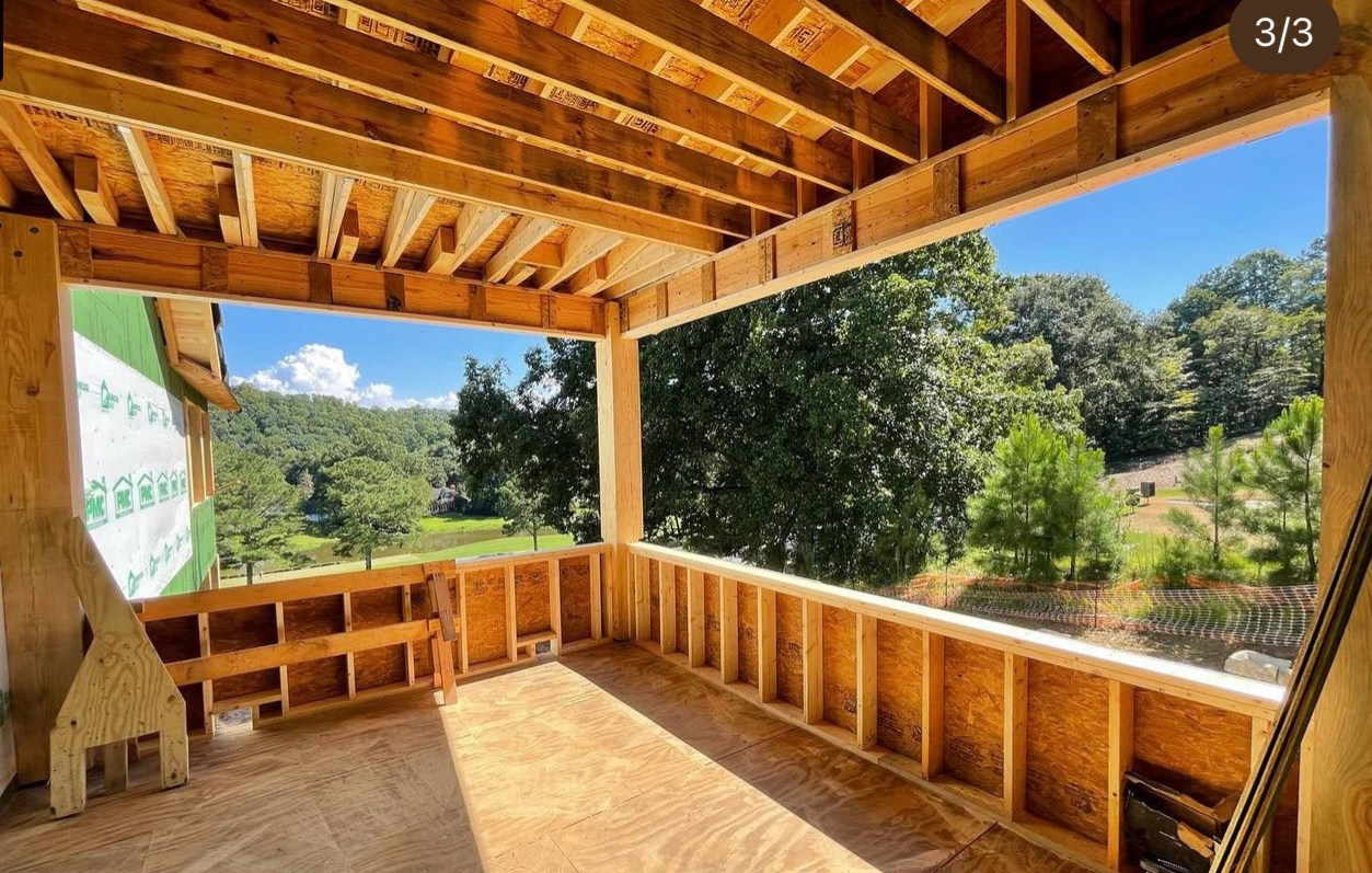 The inside of a house under construction with a view of trees and a lake.