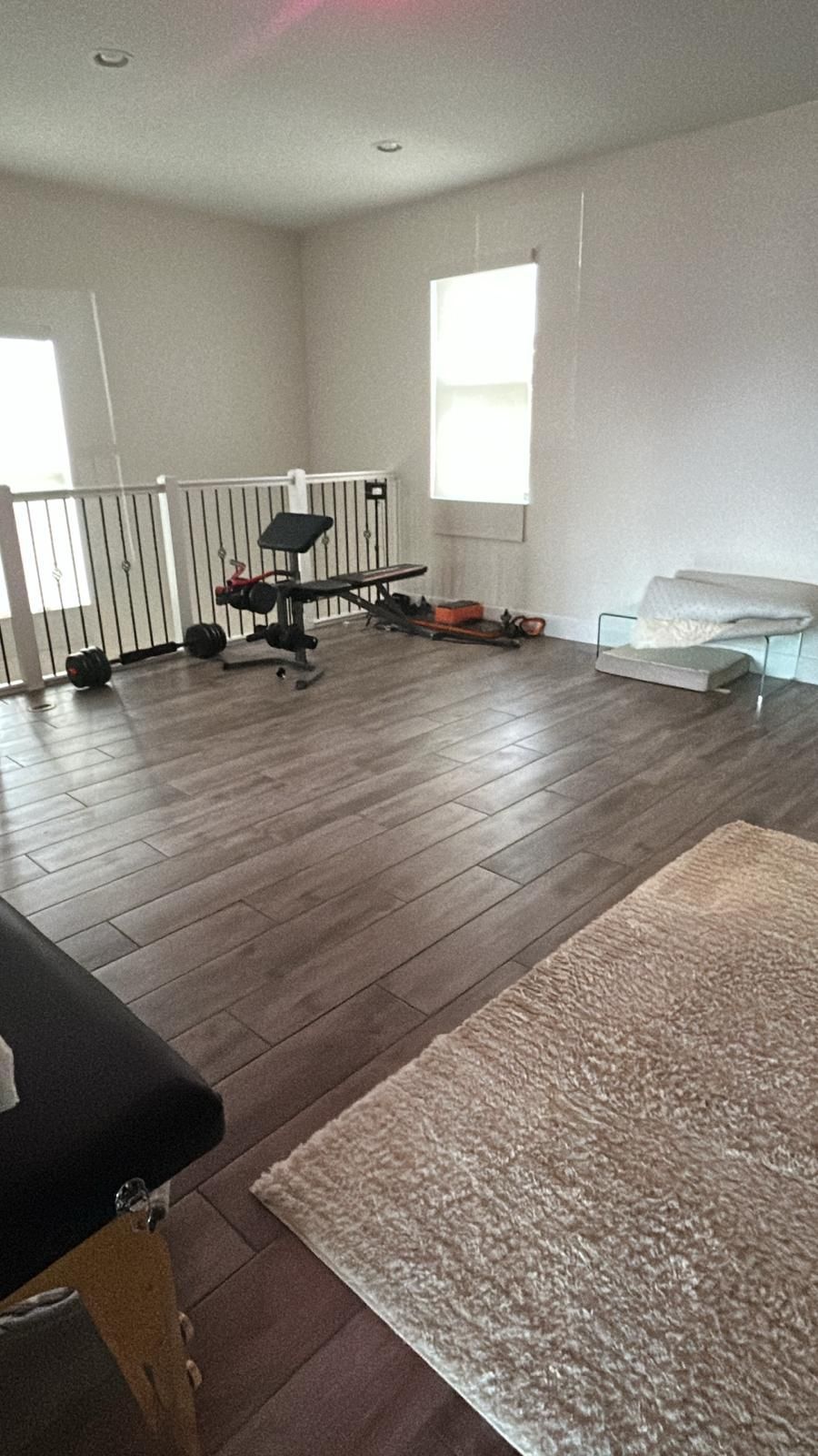A room with hardwood floors , a bench , a rug and a window.