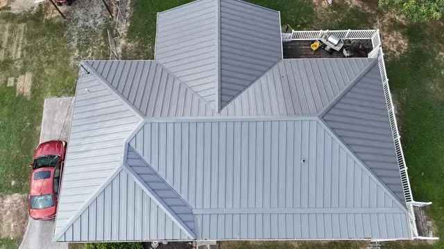 An aerial view of a house with a gray metal roof and a red car parked in front of it.