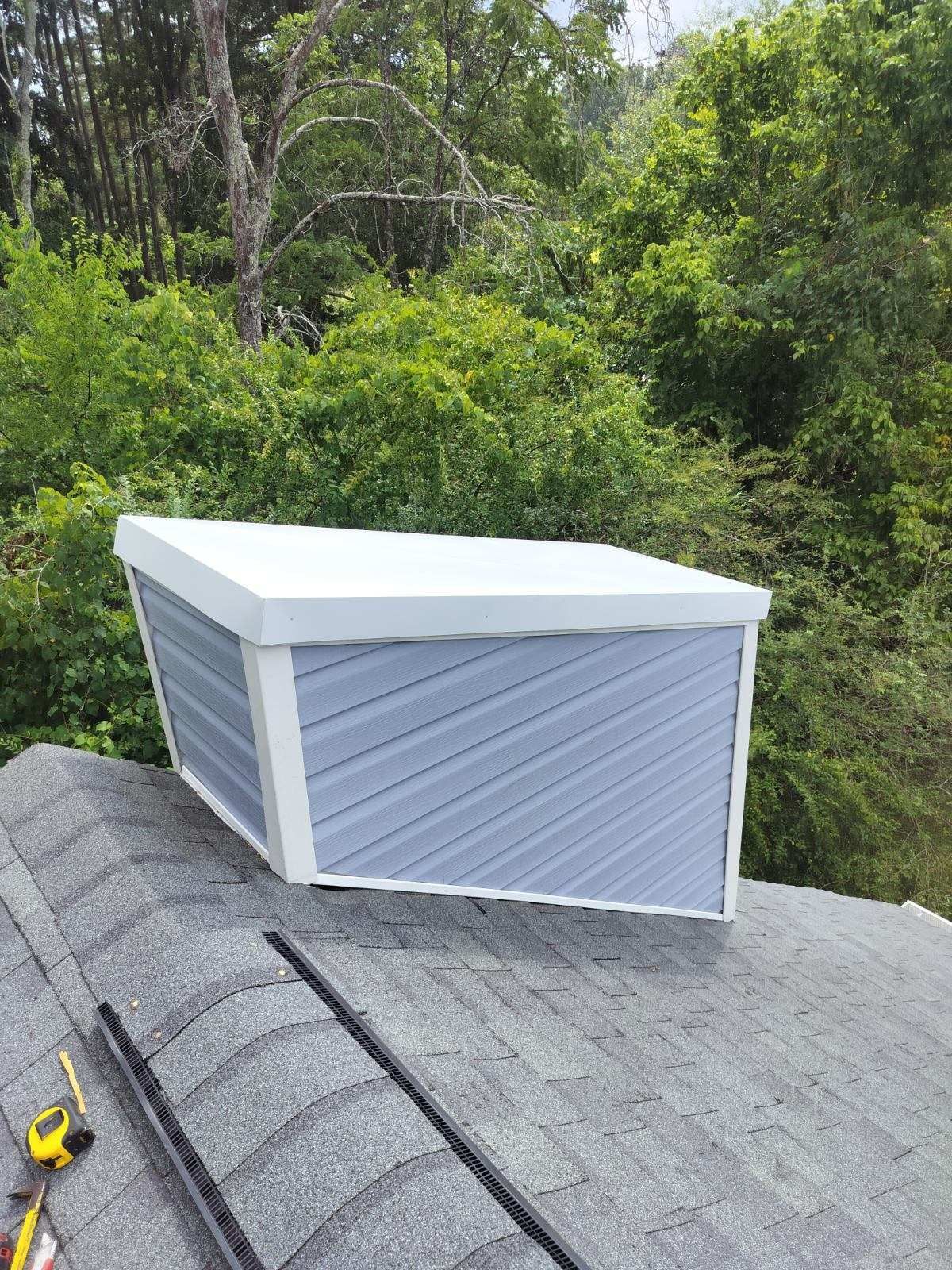 A box is sitting on top of a roof next to trees.