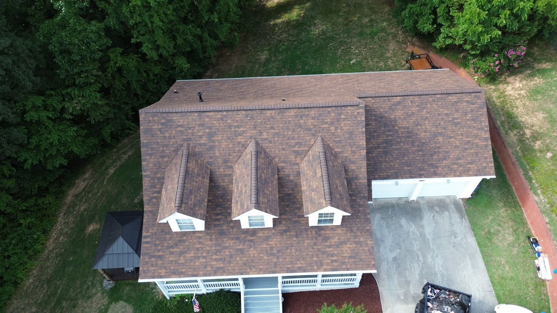 An aerial view of a house with a brown roof surrounded by trees.