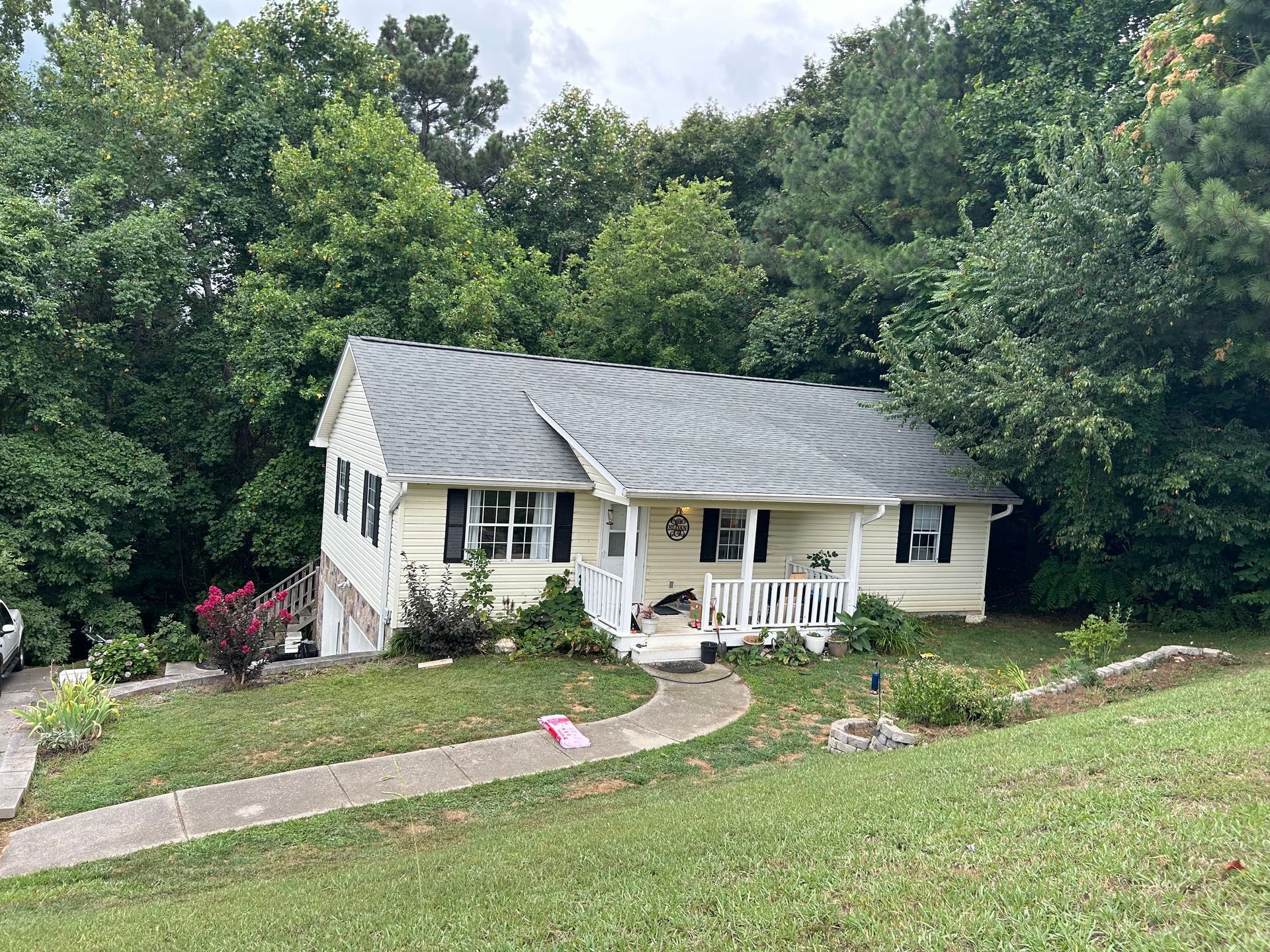 A white house with a gray roof is surrounded by trees and grass.