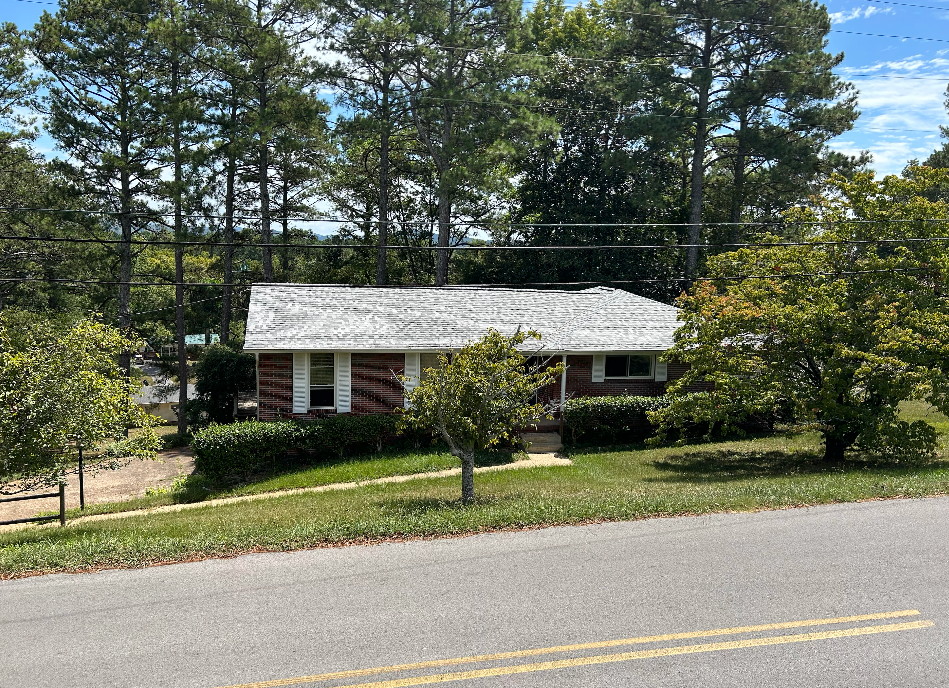 A house is sitting on a hill next to a road surrounded by trees.