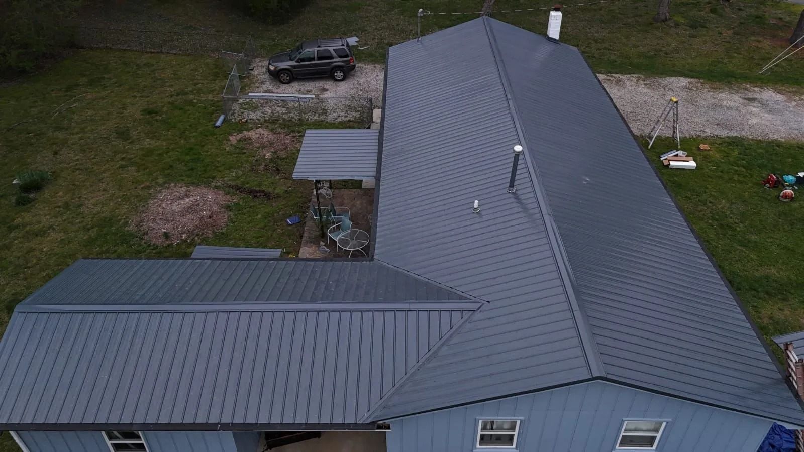 Aerial view of a blue-sided house with a dark gray metal roof, a black truck in the yard, and a grassy area.
