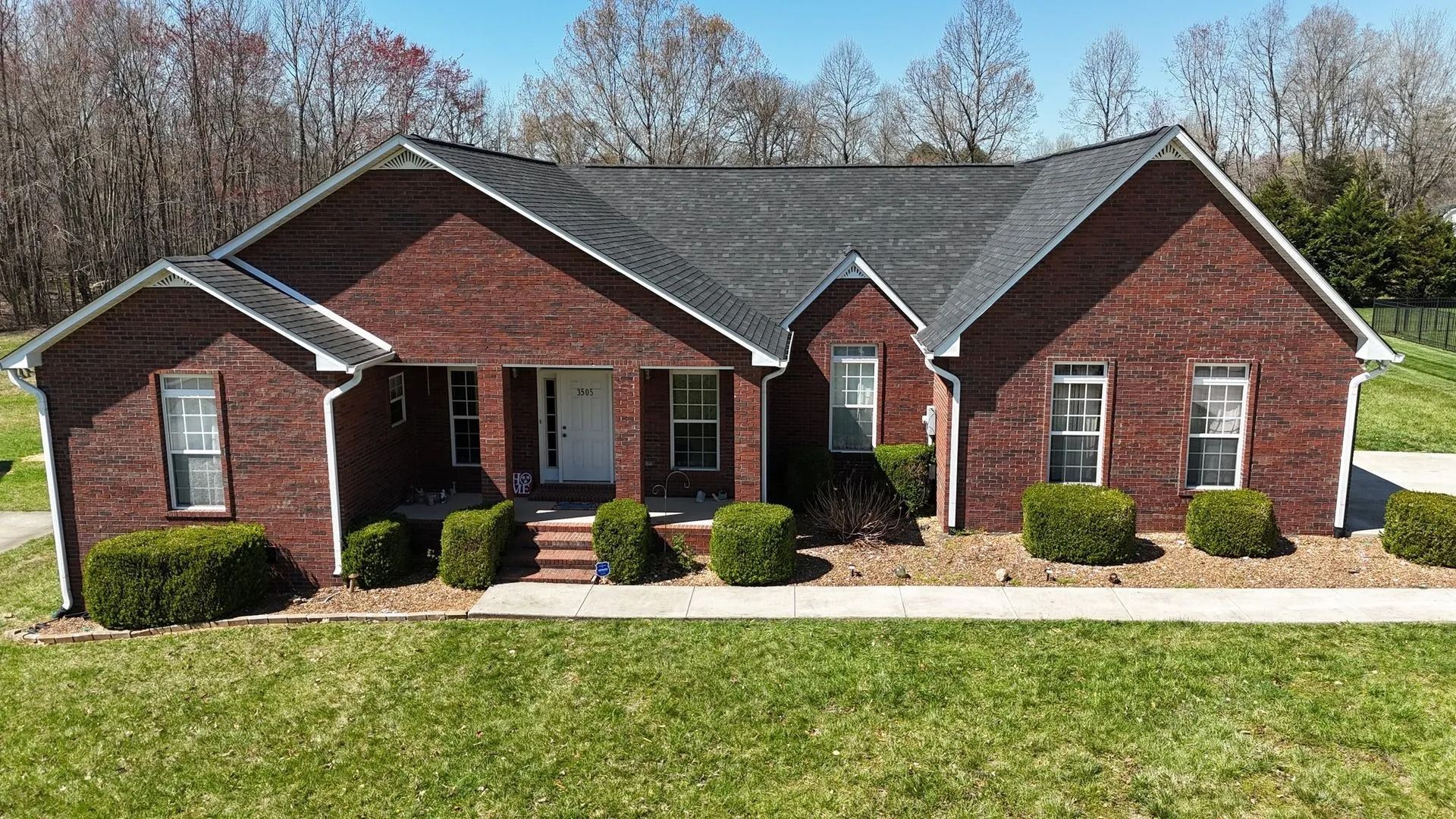 Red brick house with dark roof, windows, and manicured bushes along the front.