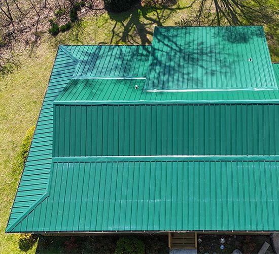 Aerial view of a blue-sided house with a dark gray metal roof, a black truck in the yard, and a grassy area.