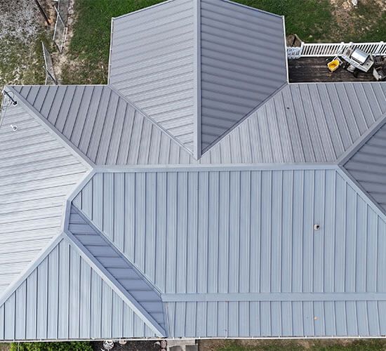 Overhead view of a house roof partially covered with turquoise underlayment, a worker installing it.