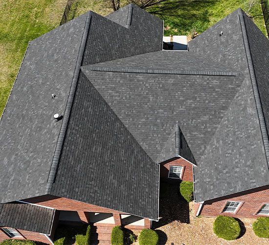 Red brick house with dark roof, windows, and manicured bushes along the front.
