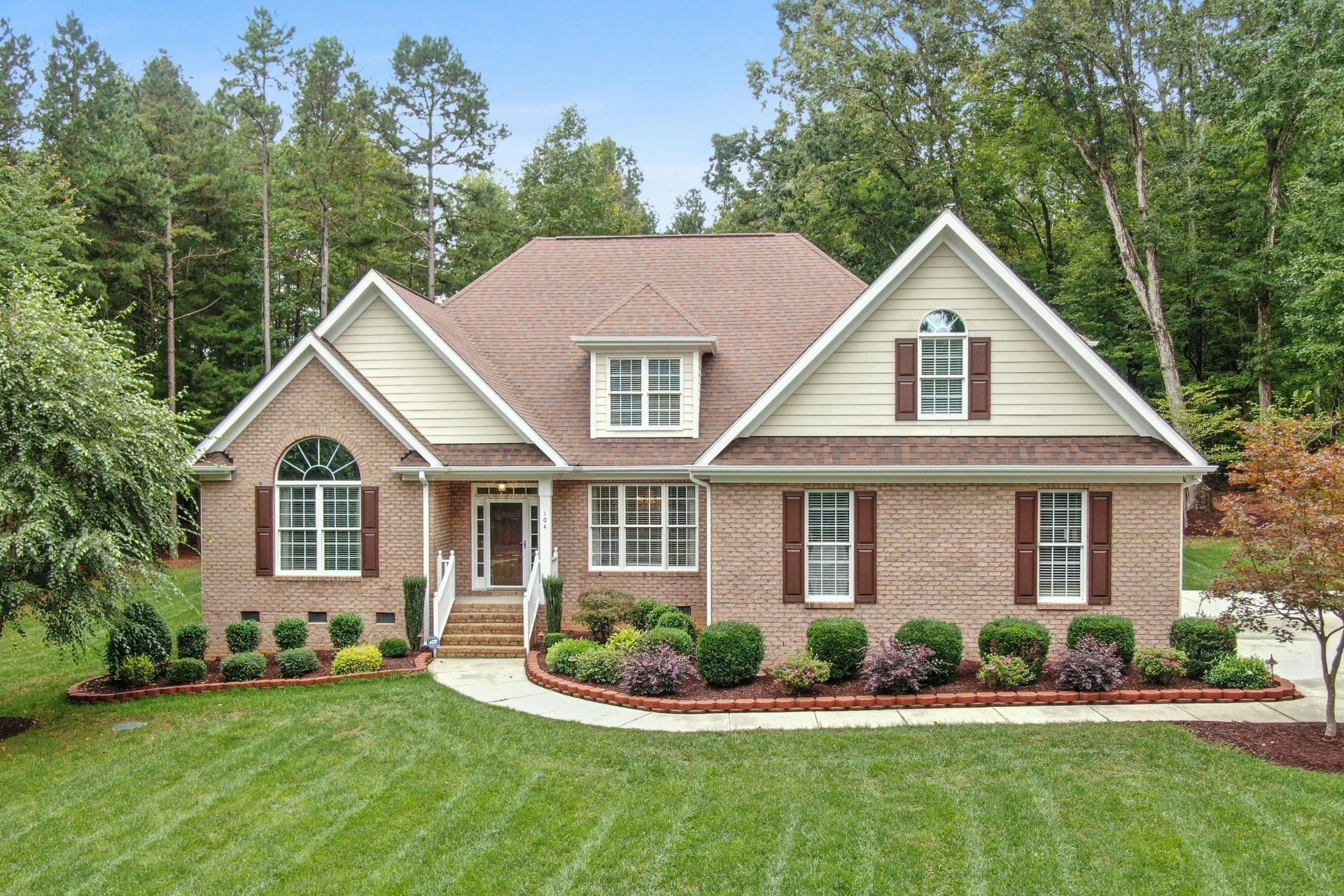 Two-story house with brown siding and deck; stairs lead up to the deck. Rocks and plants in the foreground.