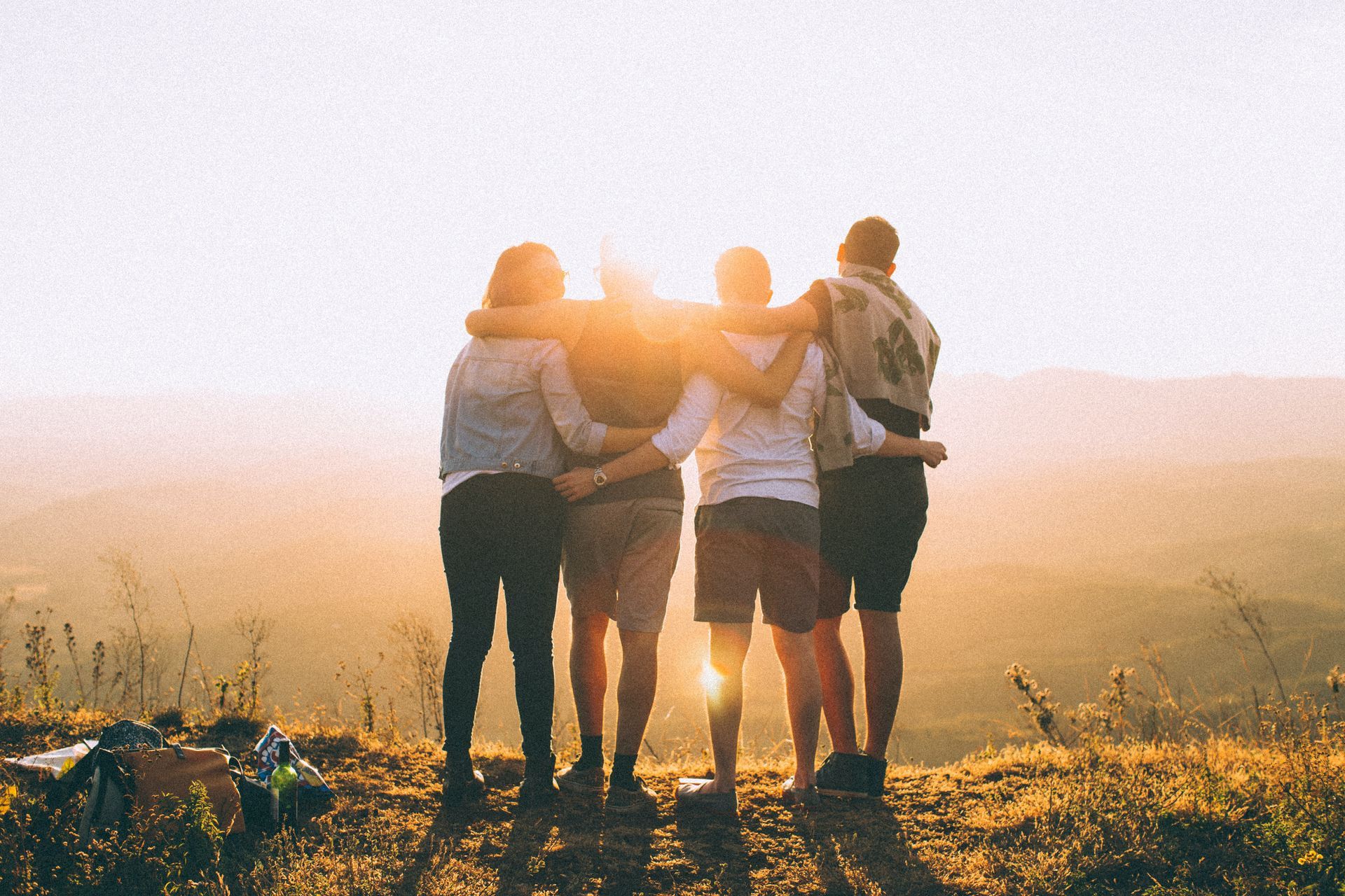 Four friends linked are in arm staring out at the sun rise with mountains in front of them
