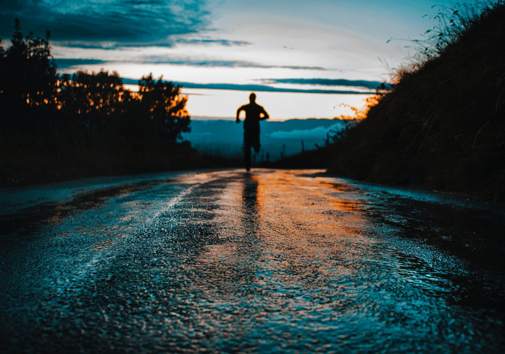 Man running down a wet road at sunset with dark clouds and forest on both sides