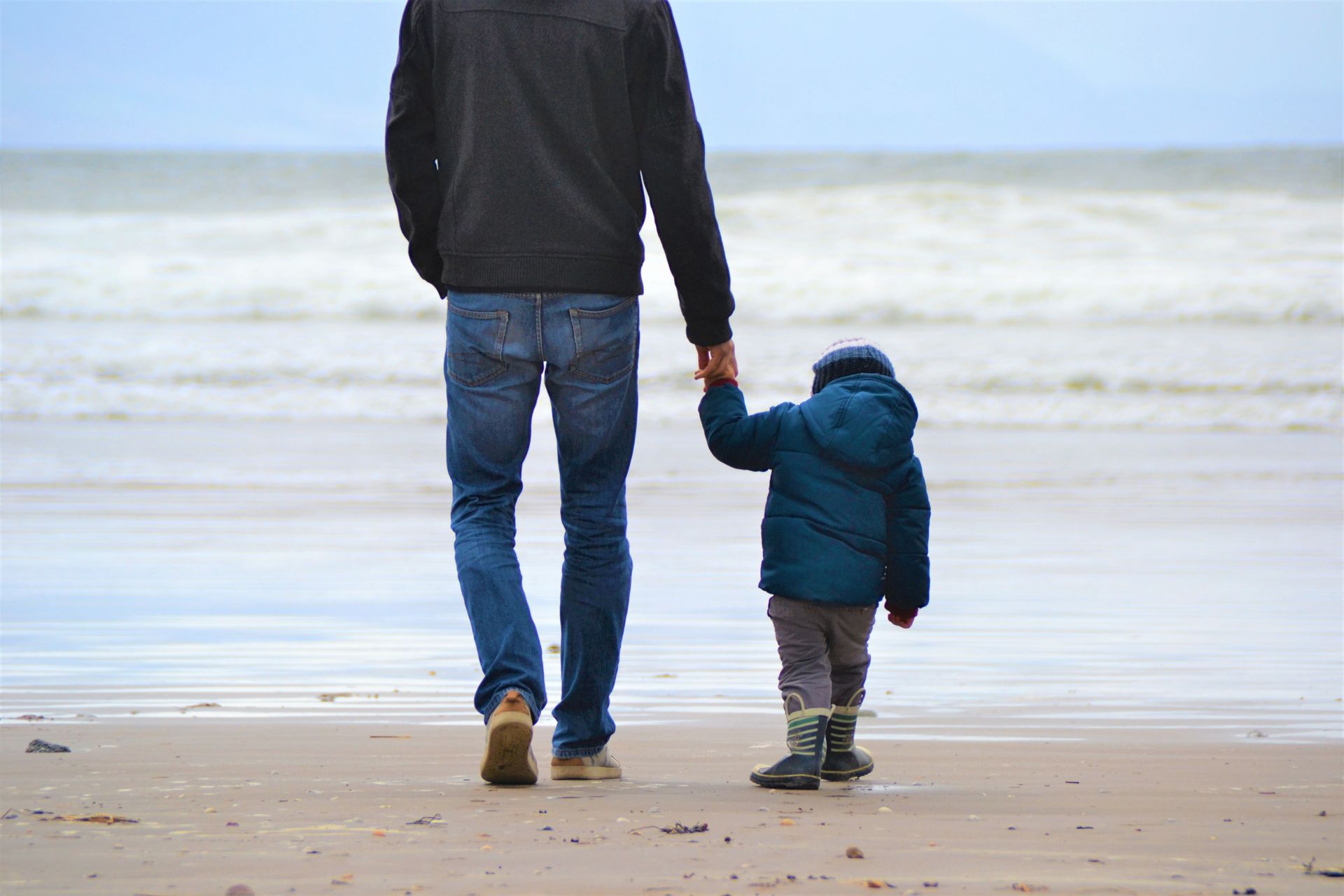 Father and son walking by the beach with a blue sky in winter wearing jackets and boots