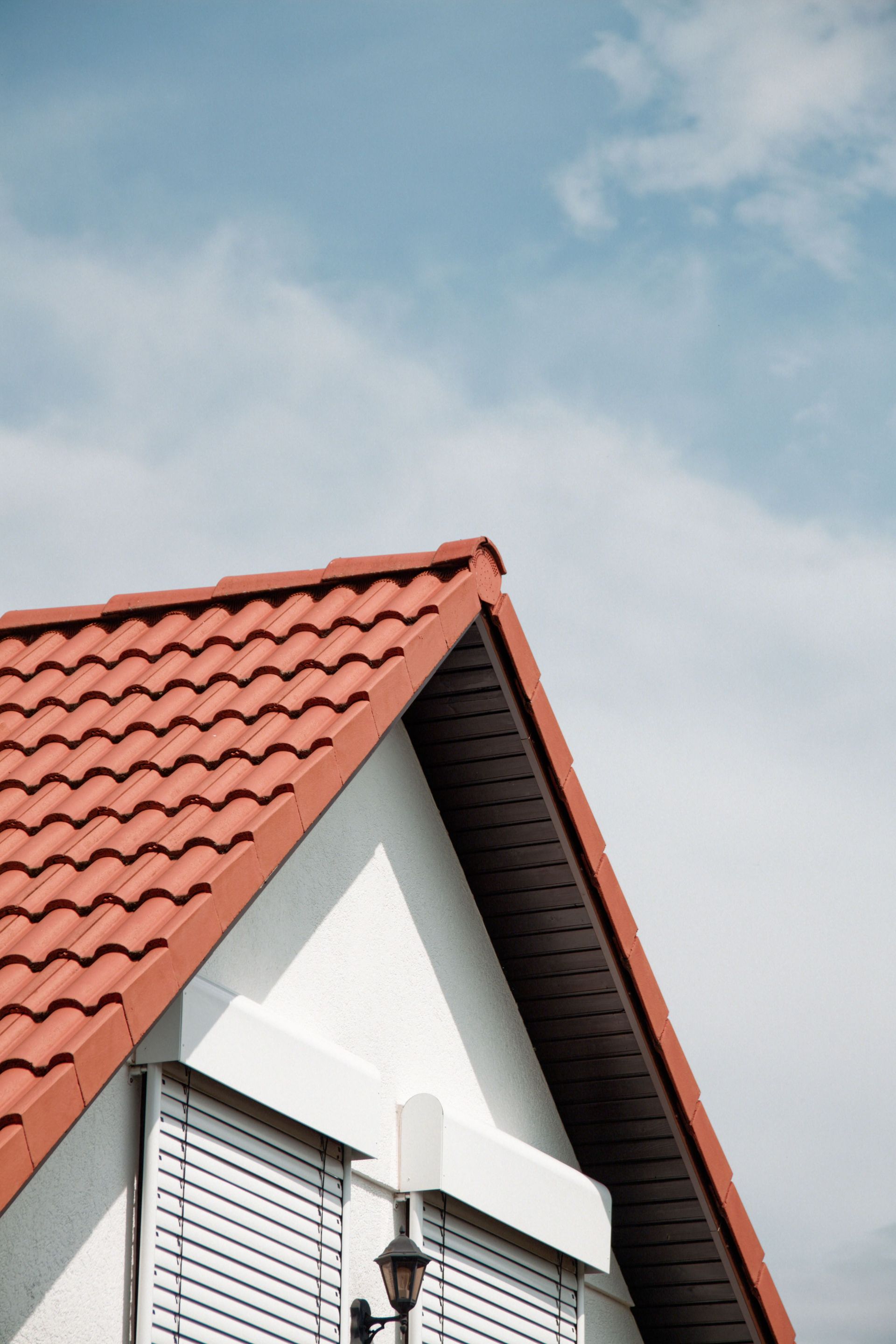 Red-tiled house roof with white gable against a cloudy blue sky