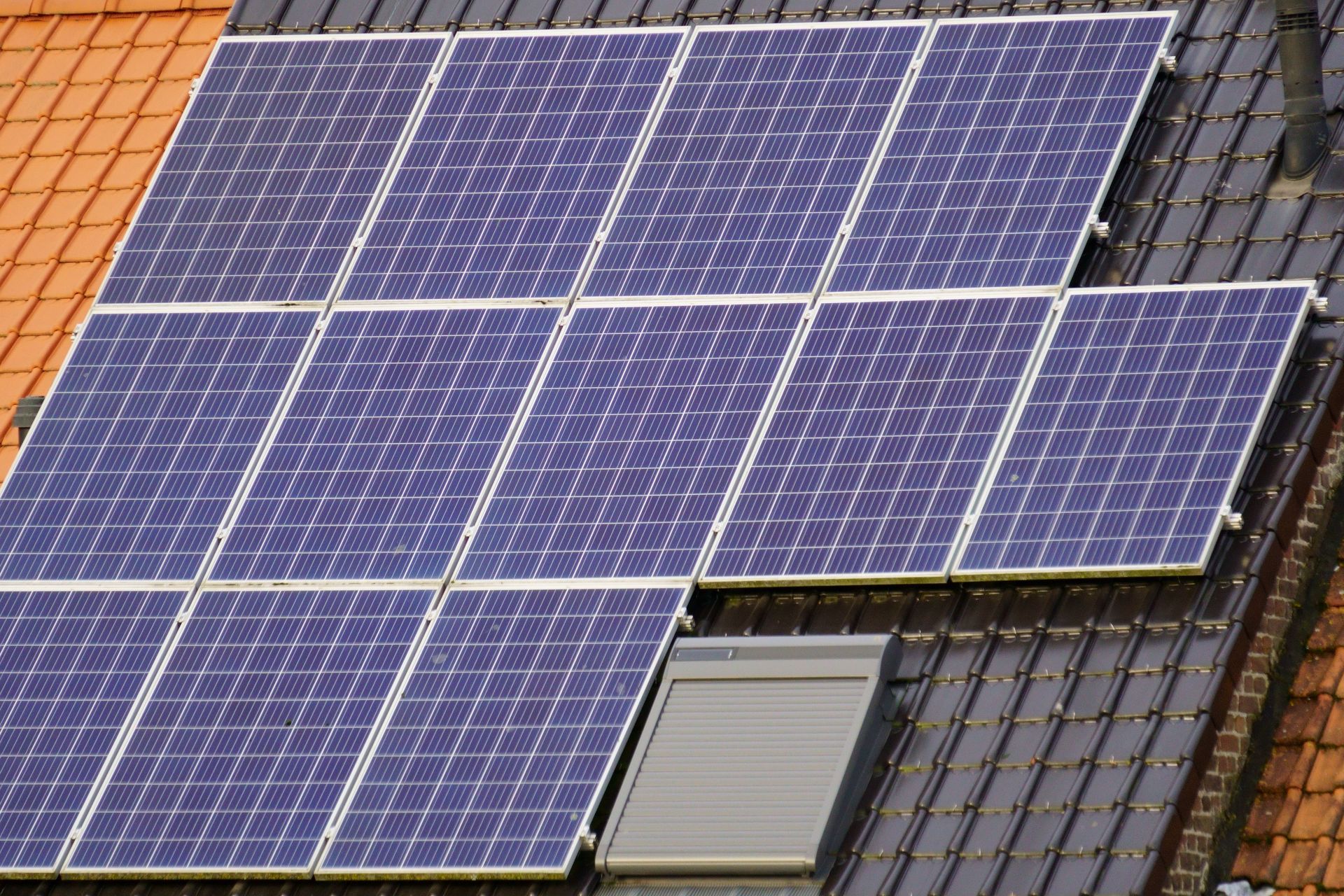 Solar panels installed on a rooftop, with blue panels over red and gray tiles.