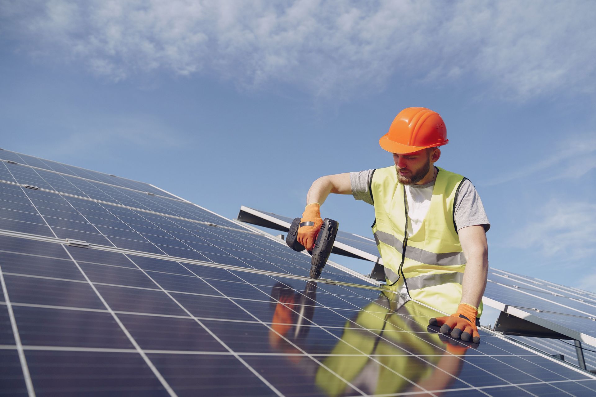 Worker in orange hard hat cleaning solar panels under a blue sky
