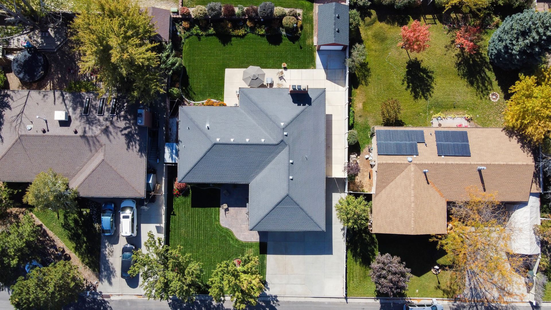 Aerial view of three suburban houses with yards, trees, and solar panels on two roofs.