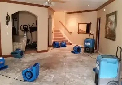 Basement with multiple blue fans drying the wet floor. Staircase and exercise equipment visible.
