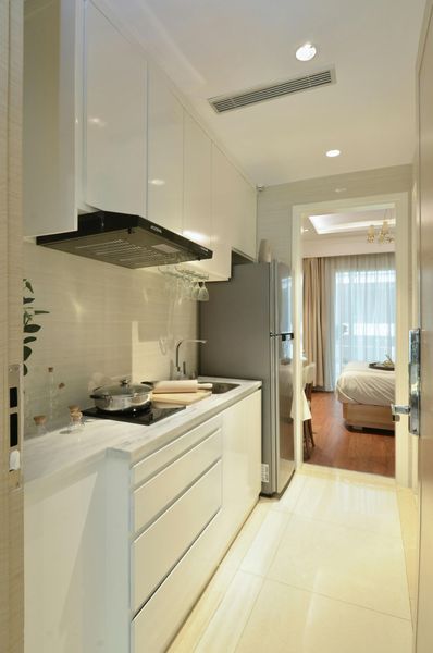 Small, modern white kitchen with appliances, leading to a bedroom.