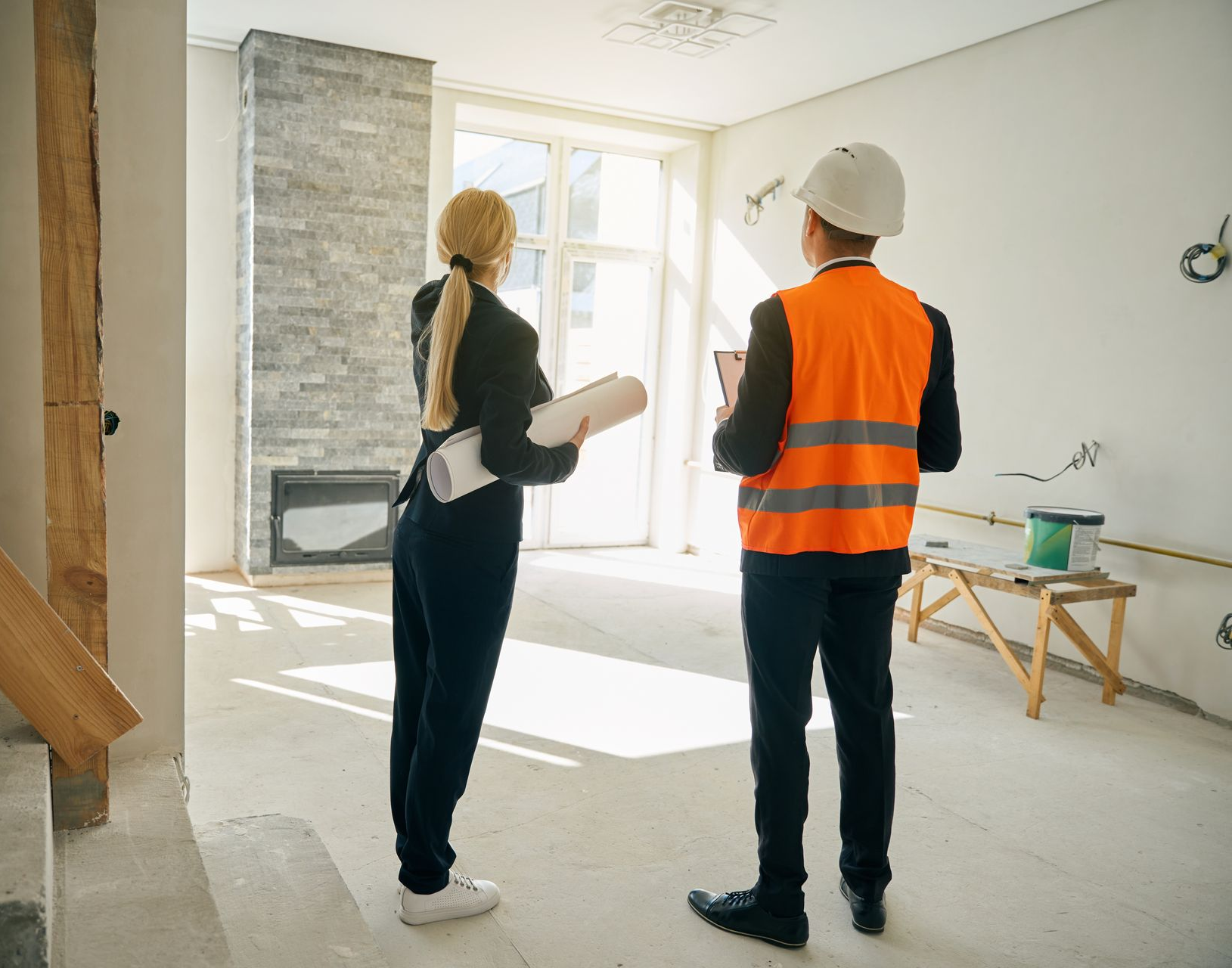 Woman and person in safety vest looking at construction site. Interior with exposed wiring.