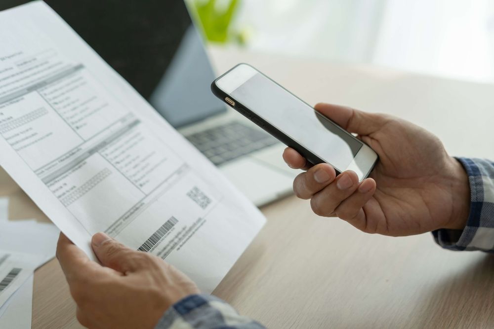 A close shot of hands holding a medical bill and a smartphone.