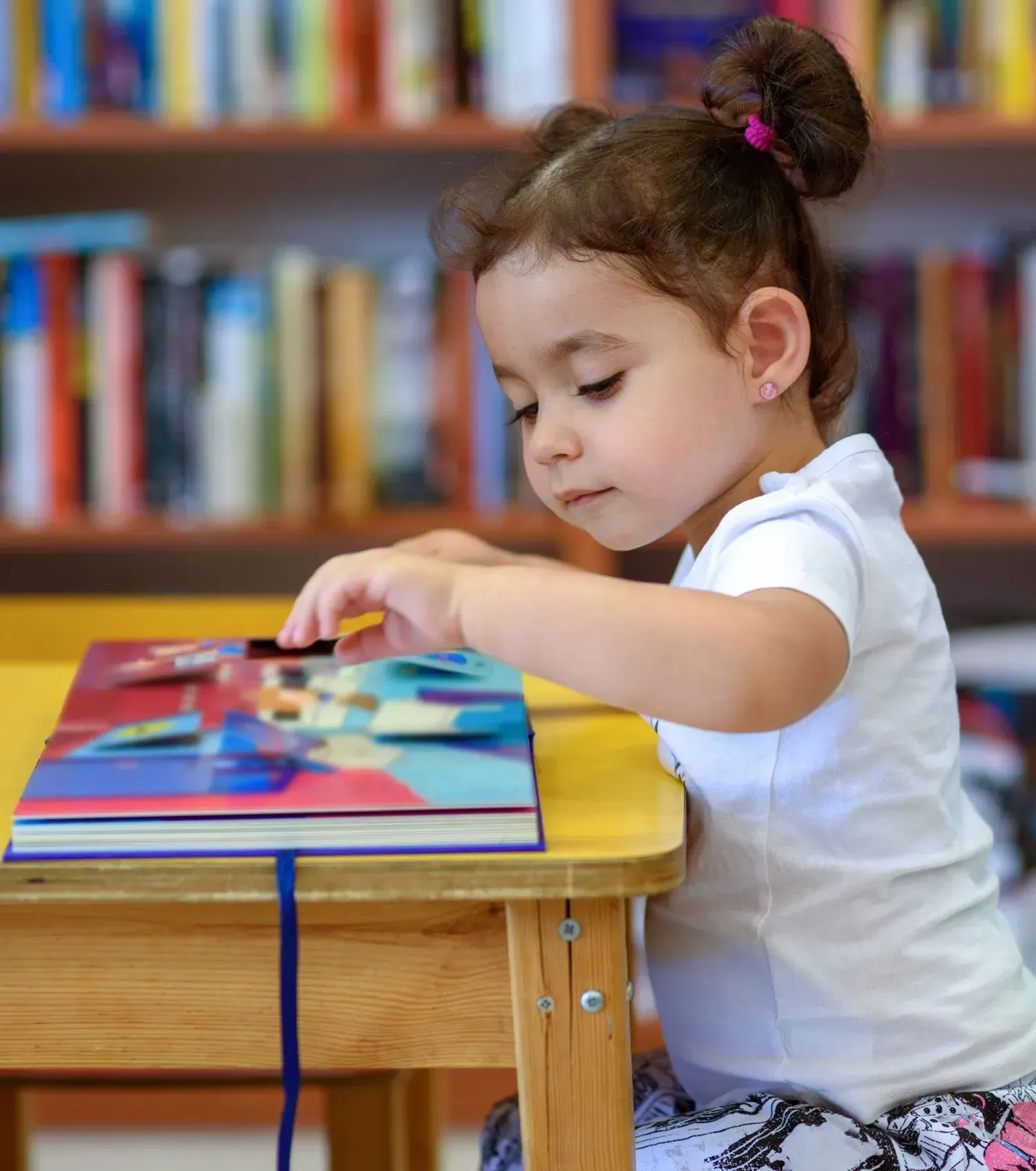 Child reading a colorful book at a small table in a library