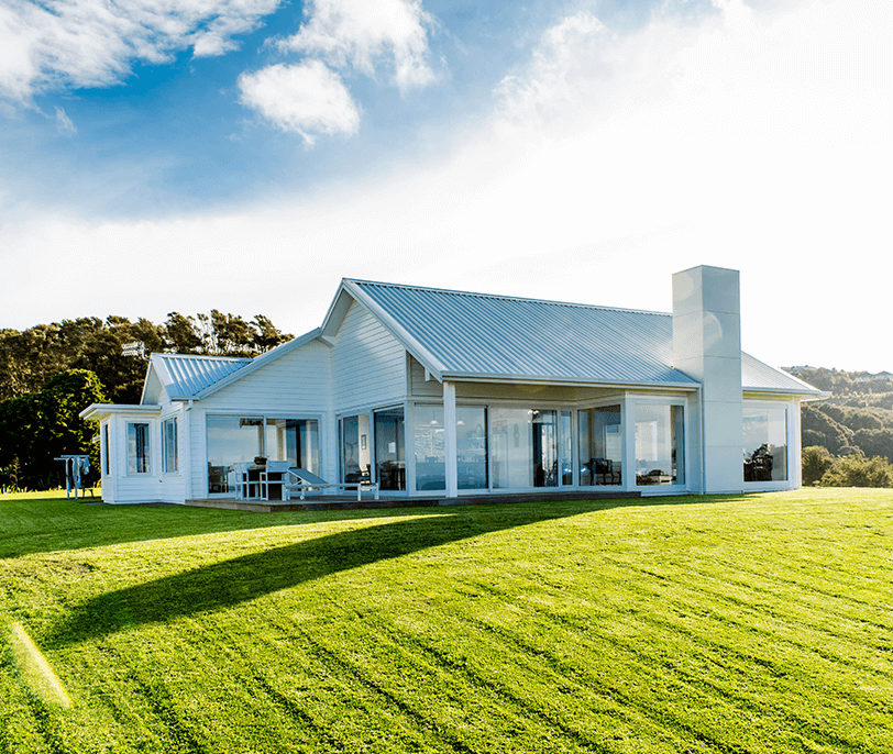 White house with large windows on a grassy hill, under a sunny sky.