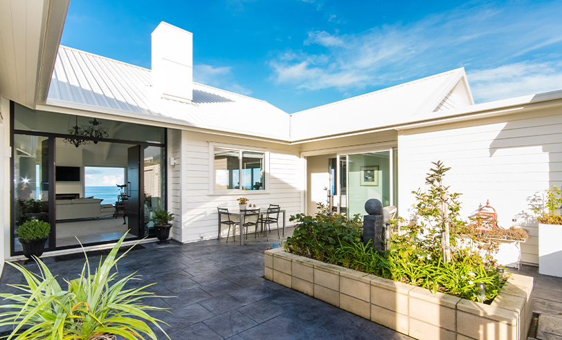 White house with blue sky, outdoor seating, plants in courtyard, ocean view.