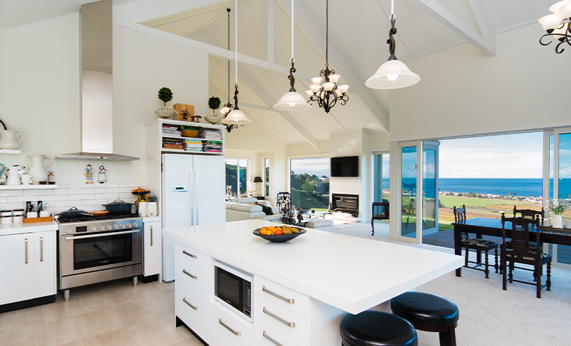 Spacious white kitchen with island, stainless steel appliances, and ocean view.