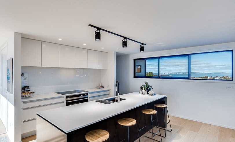 Modern kitchen with black and white cabinets, island with stools, track lighting, and a window with a scenic view.
