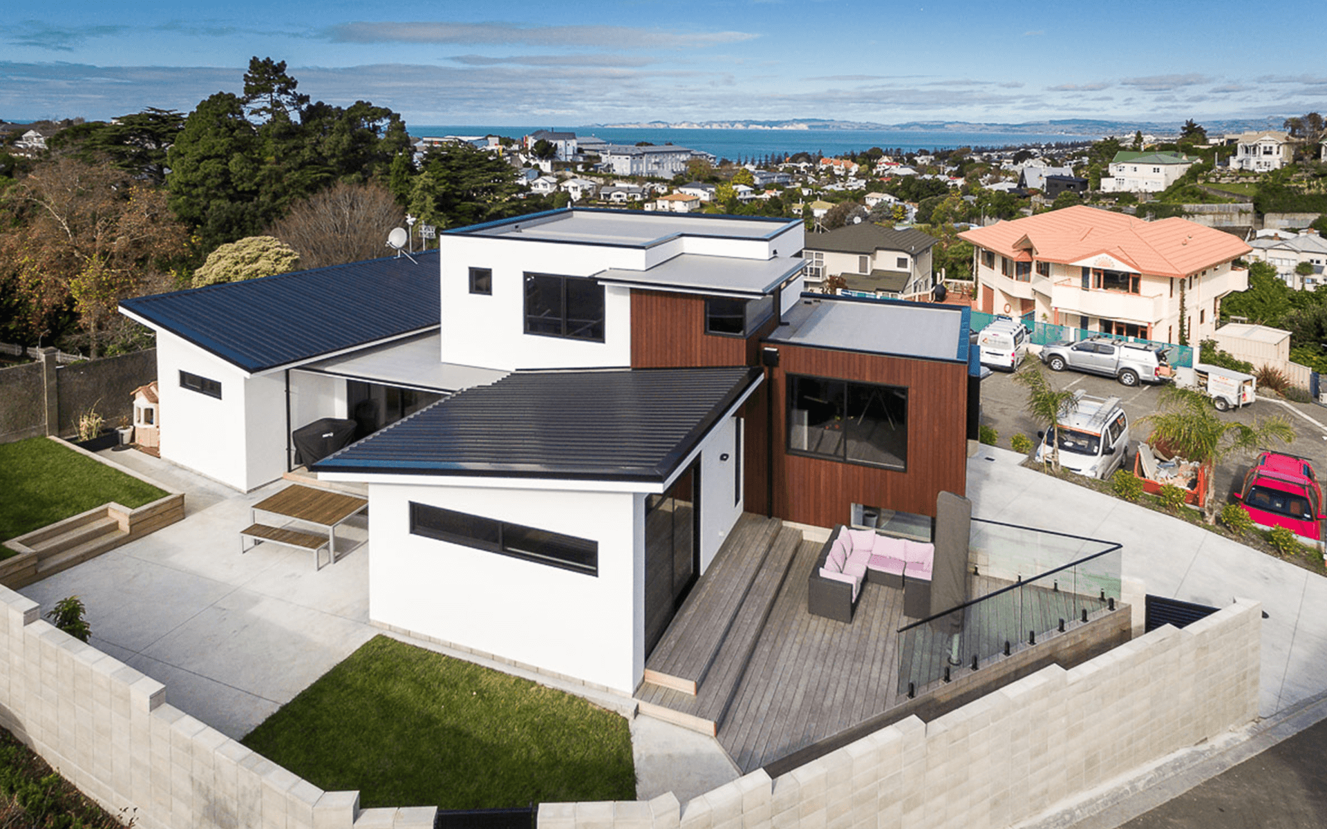 Modern white house with black accents, wooden deck, and city views in the background.