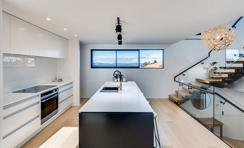 Modern white kitchen with black island, stainless steel appliances, and staircase.