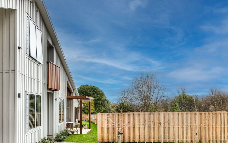 Exterior view of a modern building with vertical siding, wood accents, and a wooden fence under a blue sky.