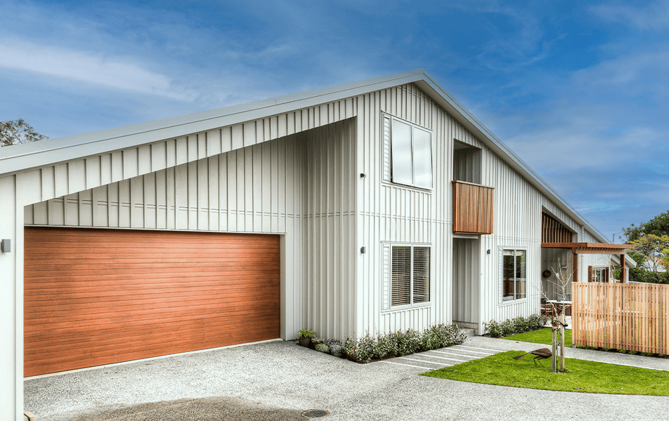 Modern white house with copper garage door, blue sky, and wooden fence.