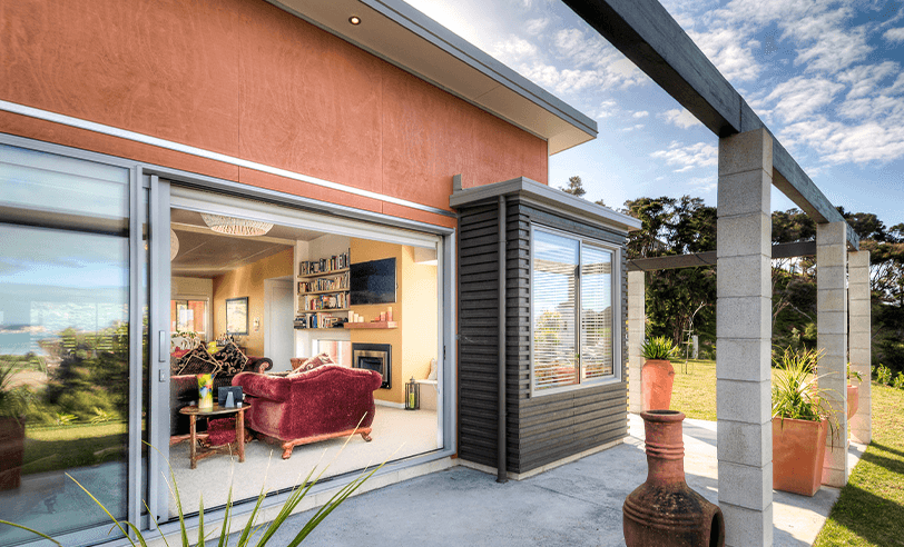 Outdoor patio with sliding glass doors to living room, orange walls, overlooking grassy area.