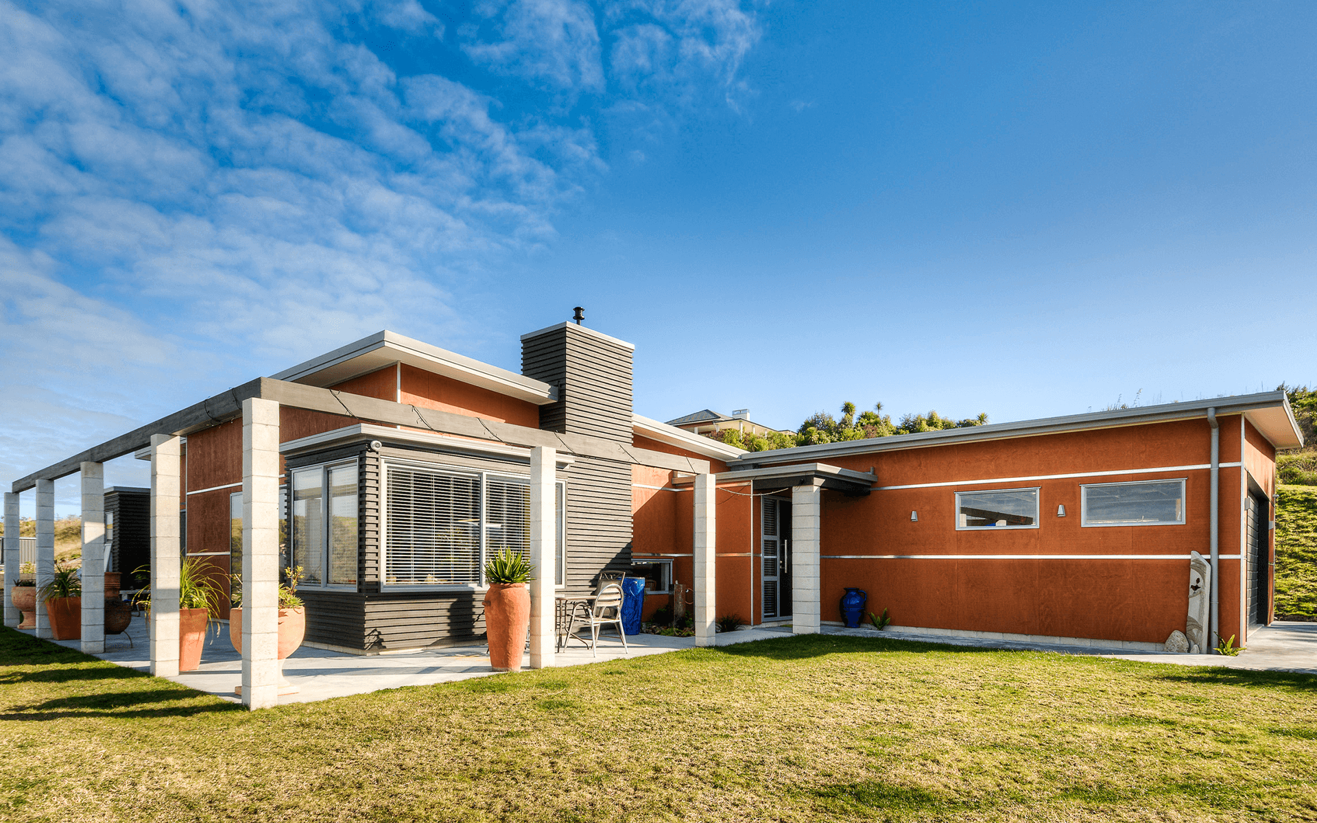 Modern orange house with a pergola, chimney, and blue sky.