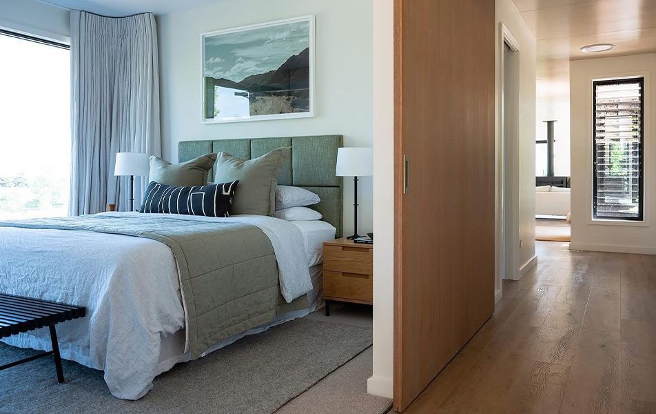 Bedroom with a bed, artwork, and a view into a hallway with a window.