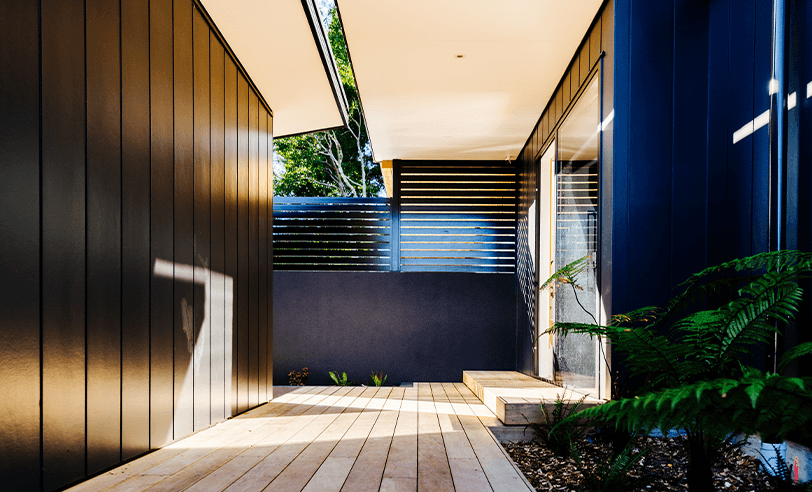 Wooden walkway with black exterior walls, leading to an open area with plants.