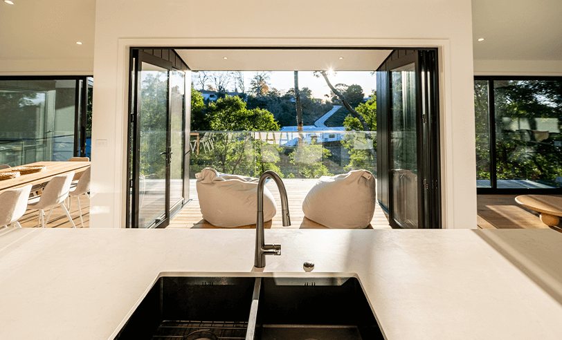 Kitchen with sink looking out to a balcony with two beanbag chairs, trees, and a clear sky.