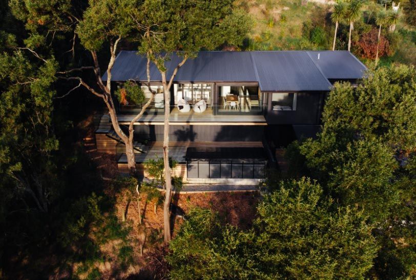 Modern house nestled in trees with a dark roof, pool and outdoor area.