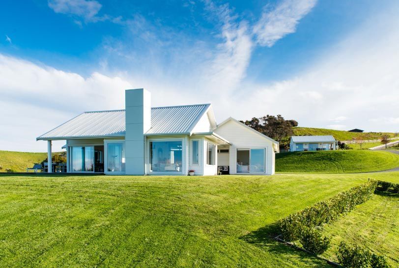 White house with large windows on a green hillside, sunny sky.