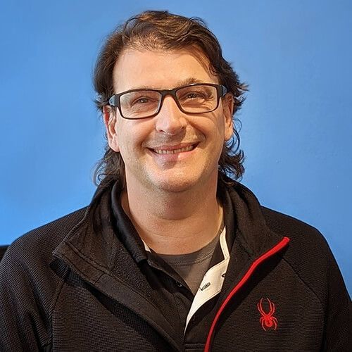 Man with glasses smiles, wearing a black jacket with a red Spider logo, against a blue background. | King's Auto Center